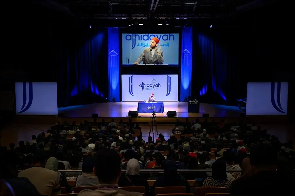 A speaker addressing a full Al-Hidayah auditorium